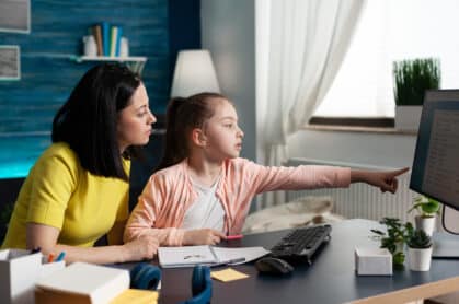 Cheerful parent sitting beside daughter doing school homework together
